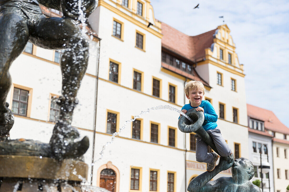 Junge sitzt auf einer Brunnenfigur am Brunnen vor dem Rathaus, Torgau, Sachsen, Deutschland, Europa