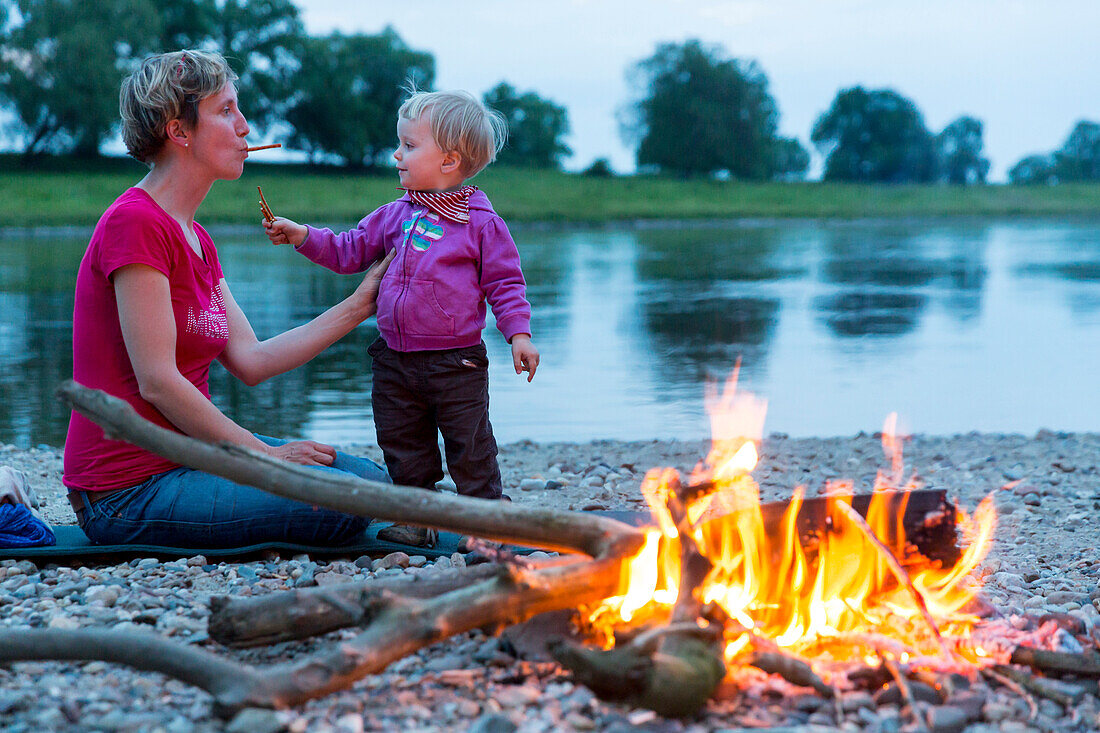 Mother and daughter making bread on a stick on the campfire, Camping along the river Elbe, Family bicycle tour along the river Elbe, adventure, from Torgau to Riesa, Saxony, Germany, Europe