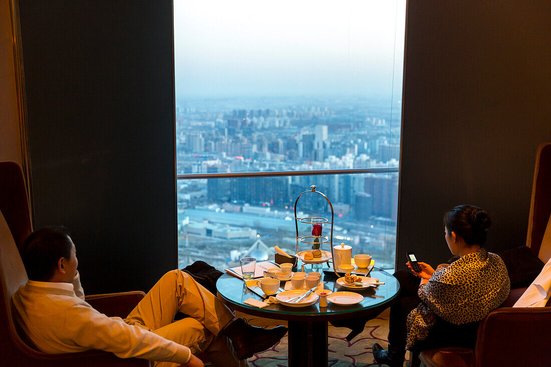 Gäste genießen Ausblick über Peking, Dämmerung, Häusermeer, Essen, China World Trade Center, Restaurant in der oberen Etage, Mann und Frau am Tisch, prunkvoll, Luxus,  Peking, China, Asien