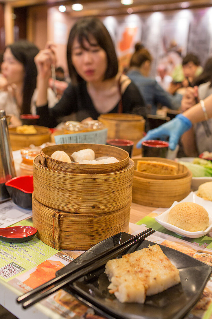 typical dim sum in bamboo steamers, chop sticks, young woman, restaurant, dining, Chinese food in Hong Kong, China, Asia