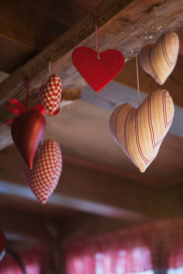 Red heart decorations in felt, fabric and metal hanging from a wooden ceiling beam, Filzmoos, Austria