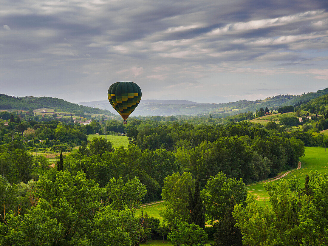 A hot air balloon flies low over a spring valley landscape, Tuscany, Italy