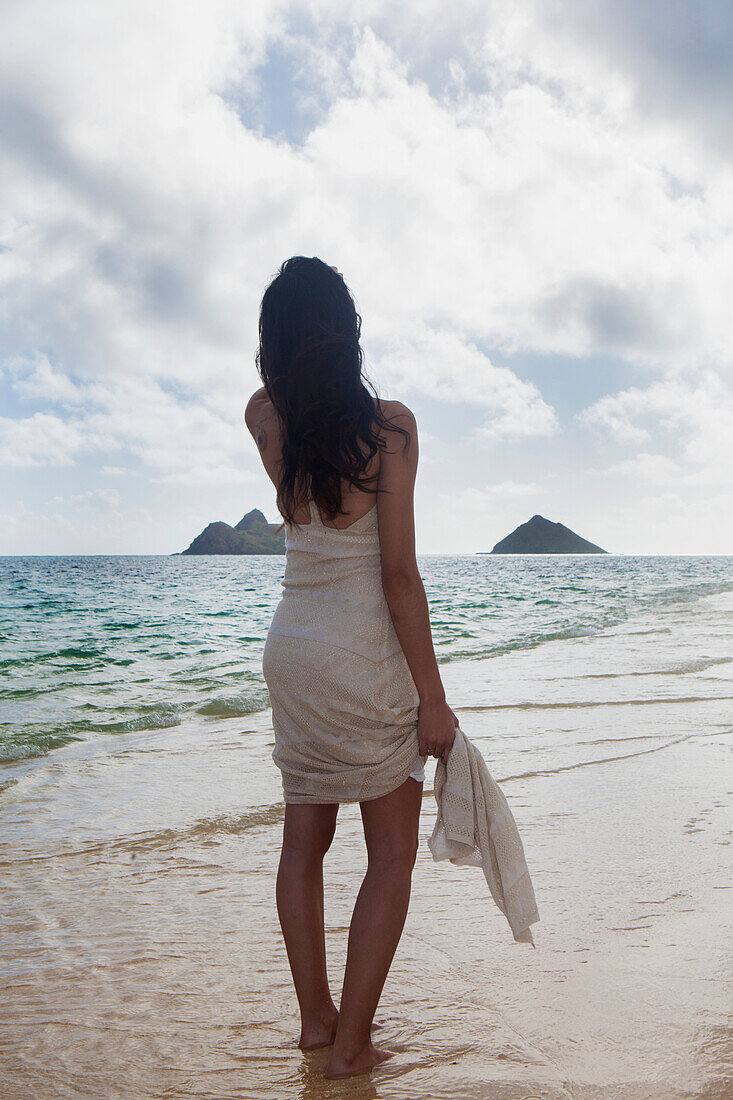 Young woman in white dress on the beach at the water's edge, Kailua, Island of Hawaii, Hawaii, United States of America