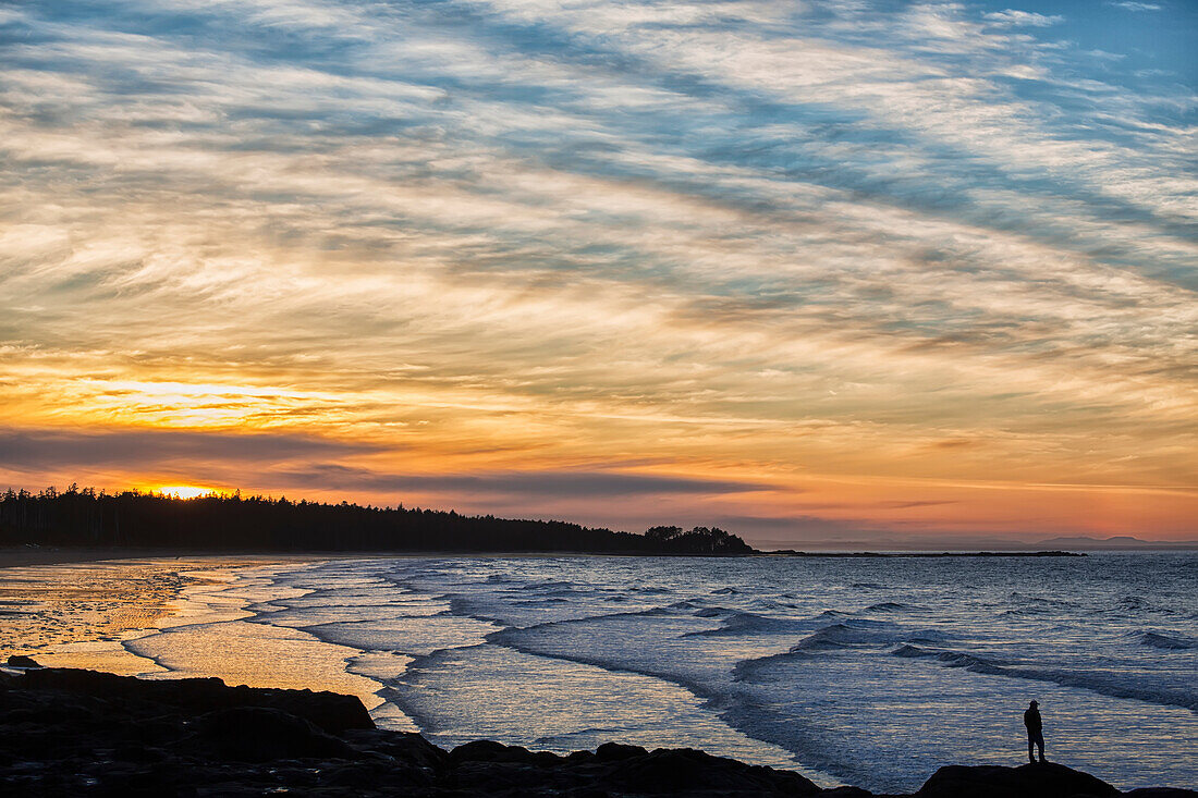 Silhouette of a person standing on a rock along the coast at sunset, Masset, British Columbia, Canada