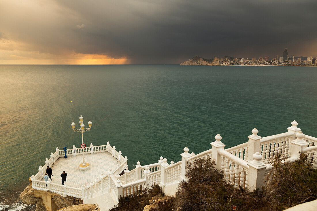 Storm clouds at sunset and a white railing leading down steps to a platform on the waterfront, Benidorm, Spain