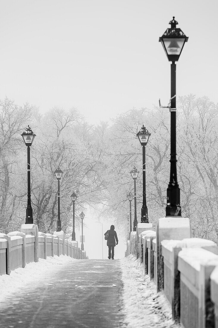 Woman walking across the Assiniboine Park foot bridge in winter, Winnipeg, Manitoba, Canada
