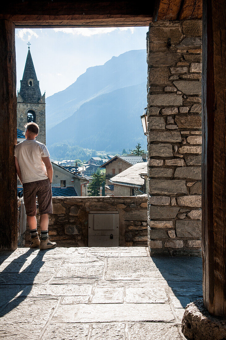 Mid-Adult Man Looking at Panoramic View from Village Doorway, Rear View, Lanslevillard, Val Cenis Vanoise, France