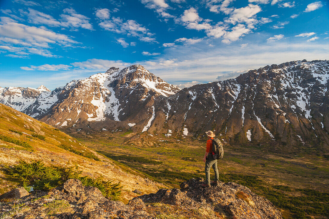 Hiker on rock outcrop overlooks Powerline Pass valley and trail, Chugach State Park, Southcentral Alaska