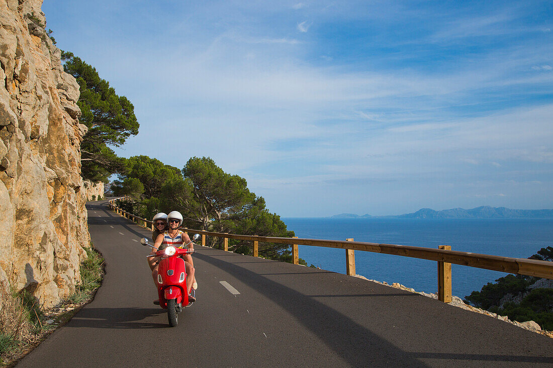 Junges Paar fährt roten Vespa Motorroller auf Straße entlang der Halbinsel Cap de Formentor mit Meer im Hintergrund, Cap de Formentor, Palma, Mallorca, Balearen, Spanien