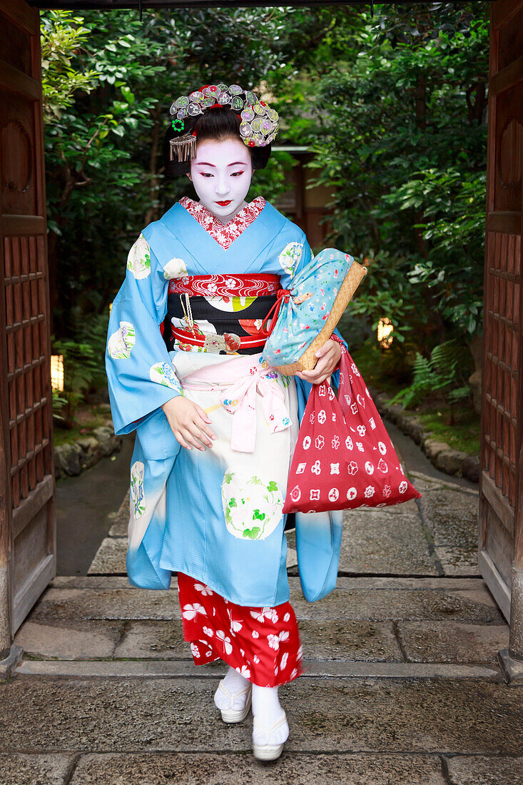 Maiko, apprentice geisha, leaves okiya geisha house through garden gate for evening appointment, Gion, Kyoto, Japan, Asia