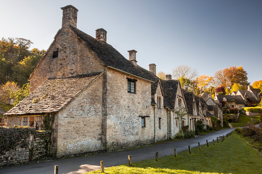 The midday sun casts its light across a row of medieval houses at Arlington Row, Bibury in Gloucestershire, Cotswolds, England, United Kingdom, Europe
