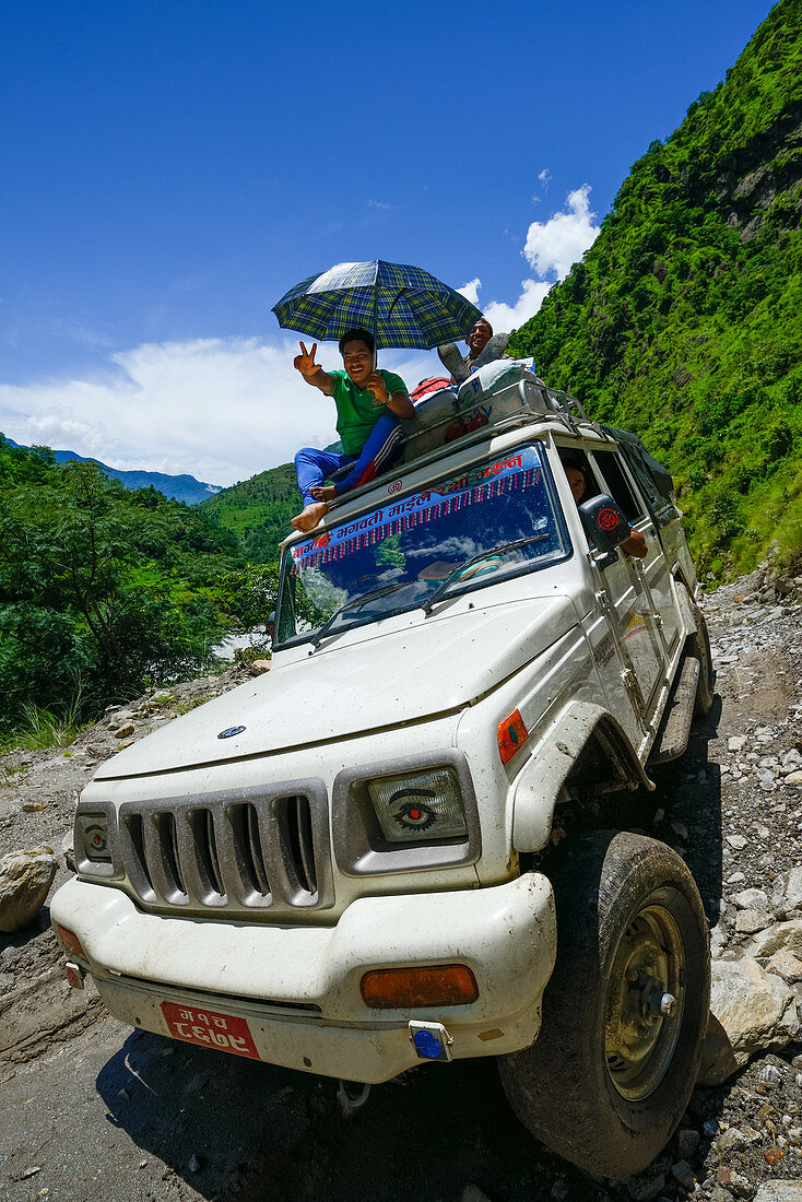 Man sitting an the roof of a 4x4 vehicle, jeep with an umbrella in the Marsyangdi-valley, Nepal, Himalaya, Asia