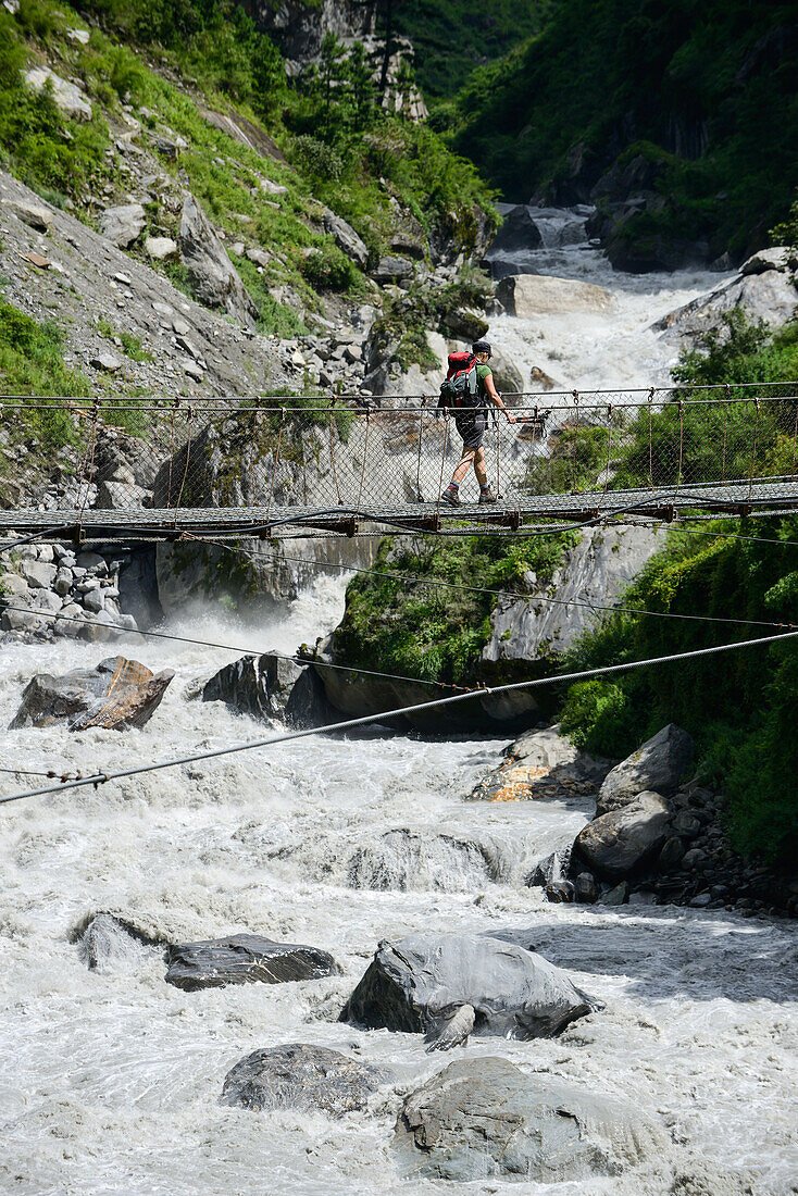 Junge Frau ueberquert den Marsyangdi Fluss auf dem Annapurna Circuit Trek im Marsyangdi Tal, Nepal, Himalaya, Asien