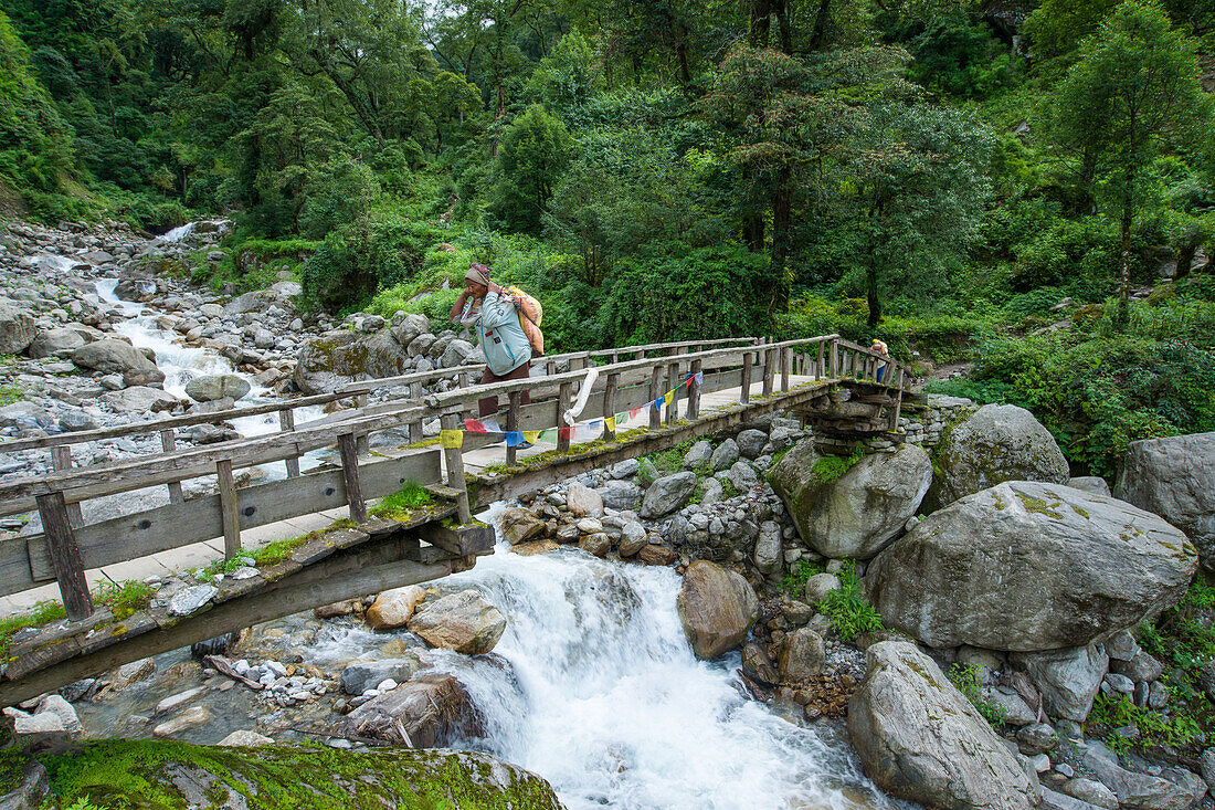 Man crossing a river on a wooden bridge on the Annapurna Circuit Trek in the Marsyangdi valley, Nepal, Himalaya, Asia