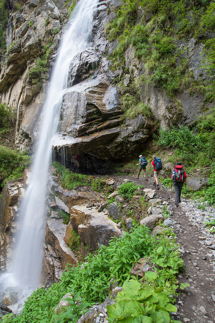 Two young women and a young man walking behind a waterfall on the Nar Phu Trek, Nepal, Himalaya, Asia