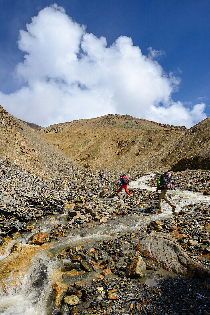 A young woman and a young man jumping over a stream on the way from Nar over Teri Tal to Mustang, Nepal, Himalaya, Asia