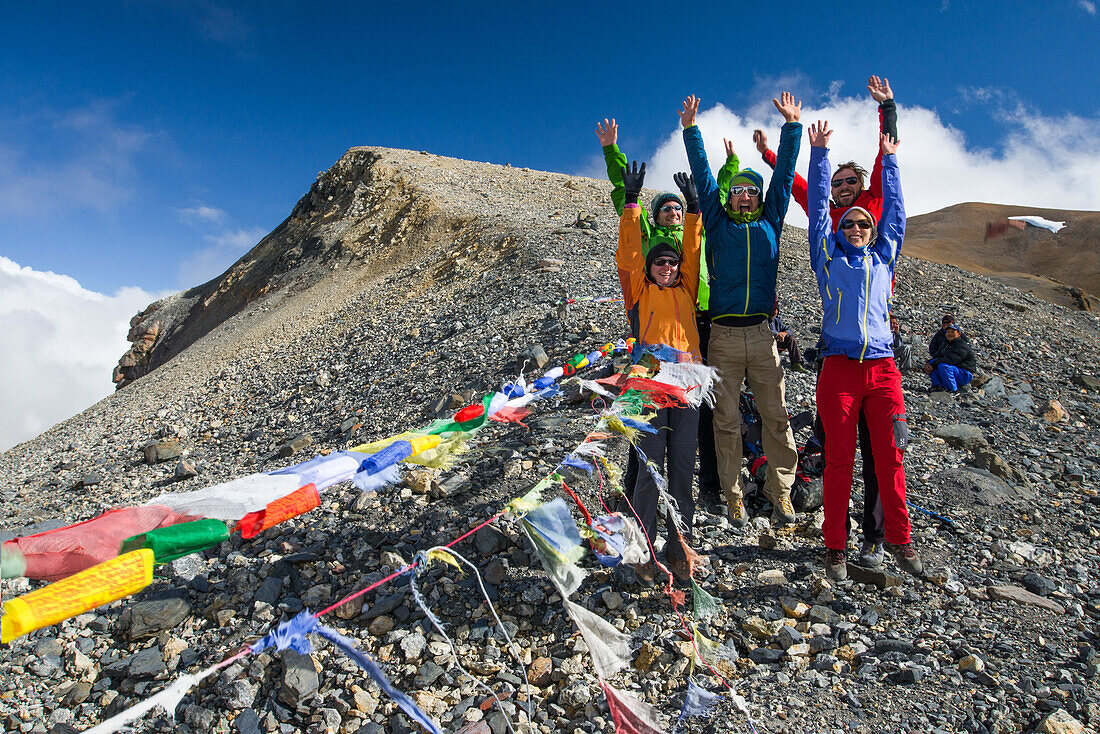 Four hikers, trekkers at Teri La Pass (5595 m) with buddhist prayer flags, on their way from Nar over Teri Tal to Mustang, Nepal, Himalaya, Asia