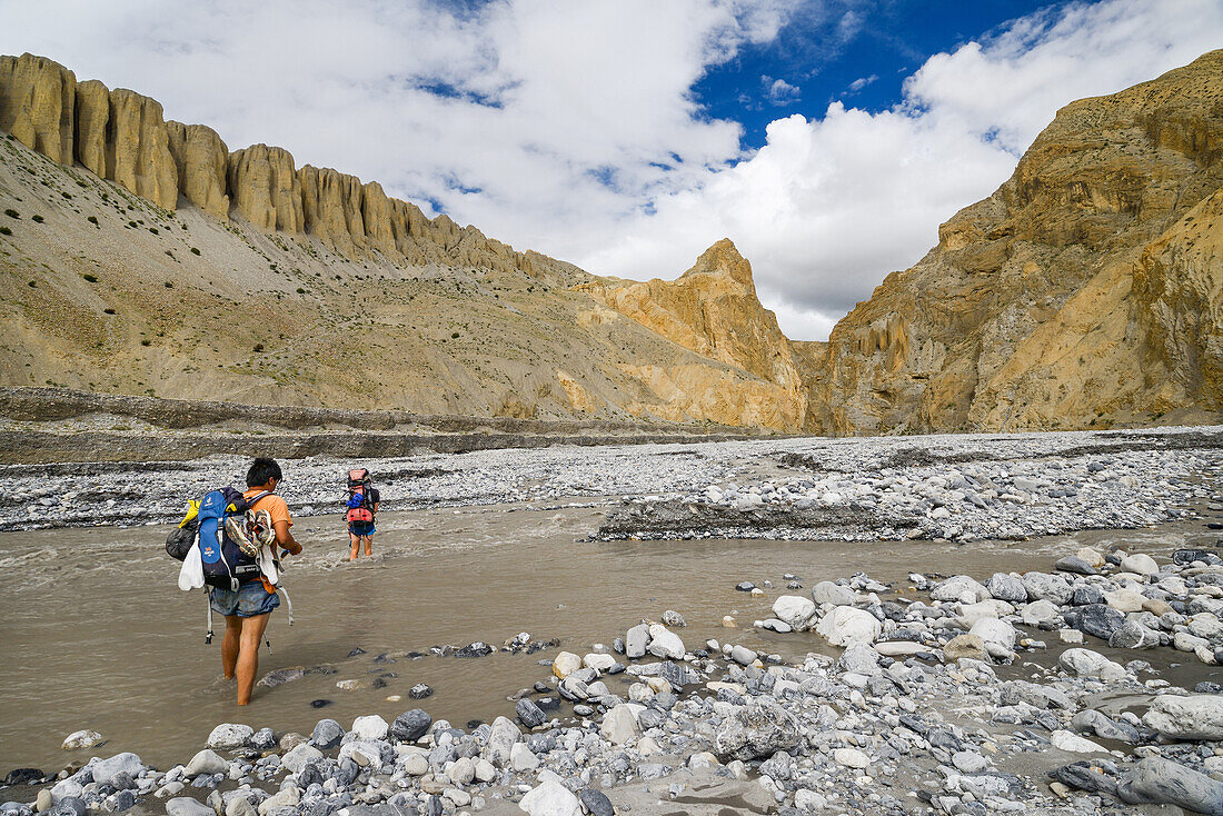 Zwei junge Maenner, Wanderer, Trekker ueberqueren Fluss Dhechyang Khola in surrealer Landschaft typisch fuer das Mustang in der Hochwueste um das Kali Gandaki Tal, dem tiefsten Tal der Welt, Mustang, Nepal, Himalaya, Asien
