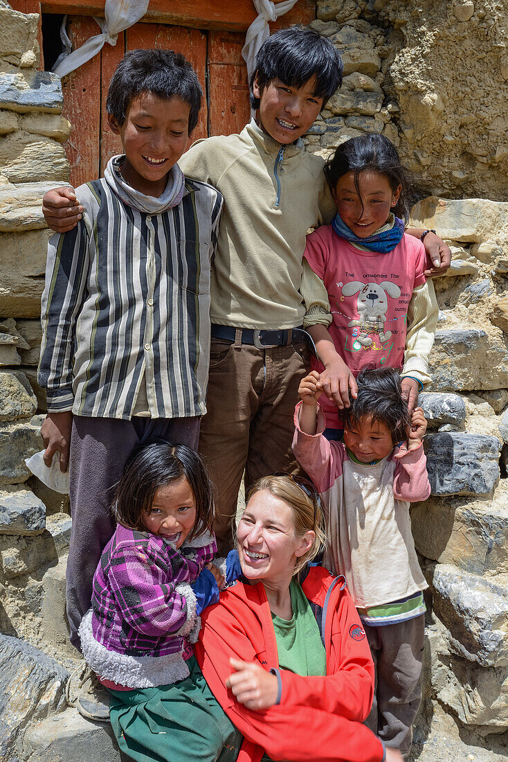 Junge Frau, Wanderer, Trekker mit einheimischen Kindern bei der Luri Gompa, Luri Gumba, buddhistisches Felsenkloster, naha Yara, Gara, Koenigreich Mustang, Nepal, Himalaya, Asien