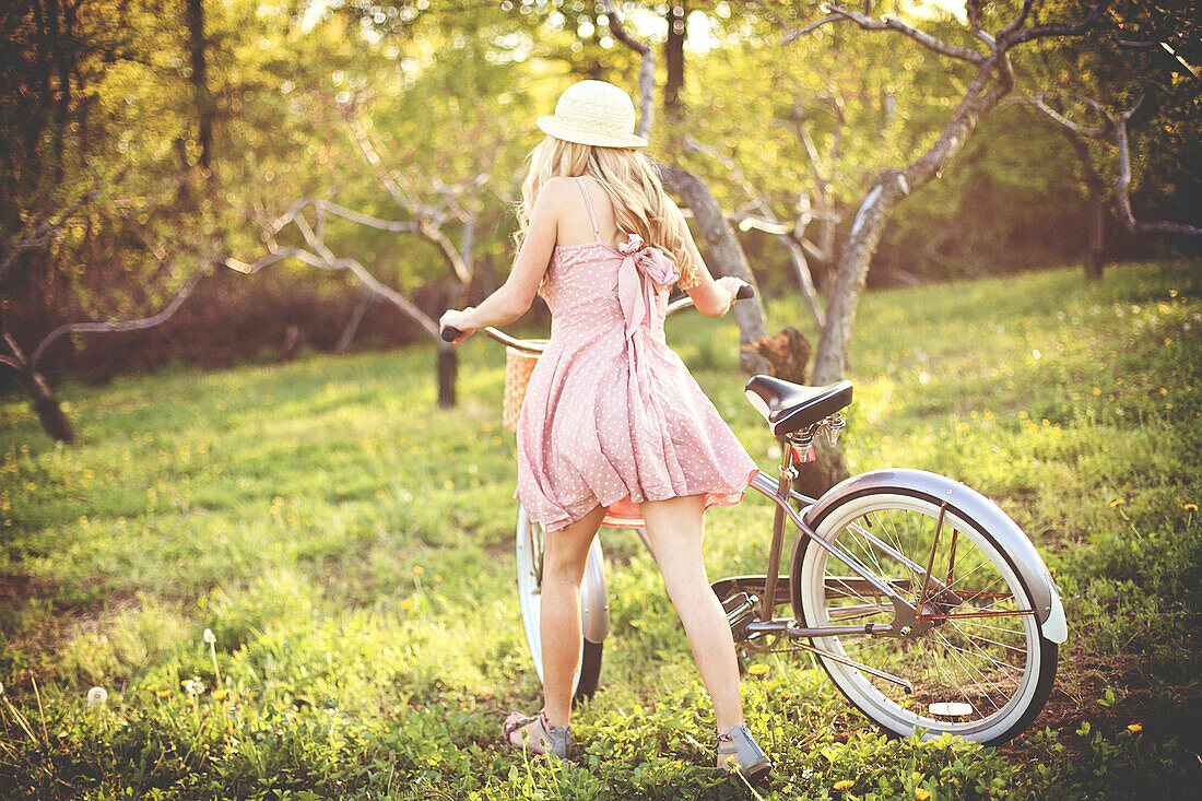 Woman pushing bicycle in rural field