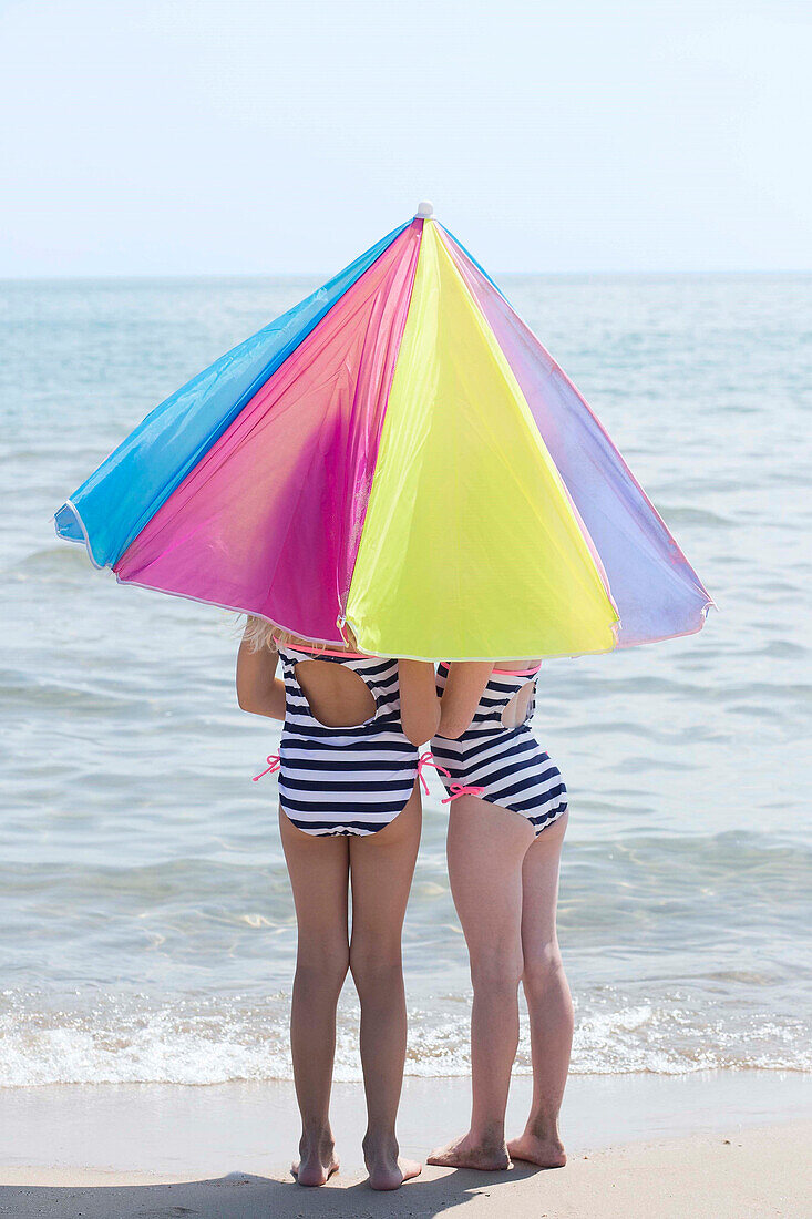Caucasian girls under umbrella on beach