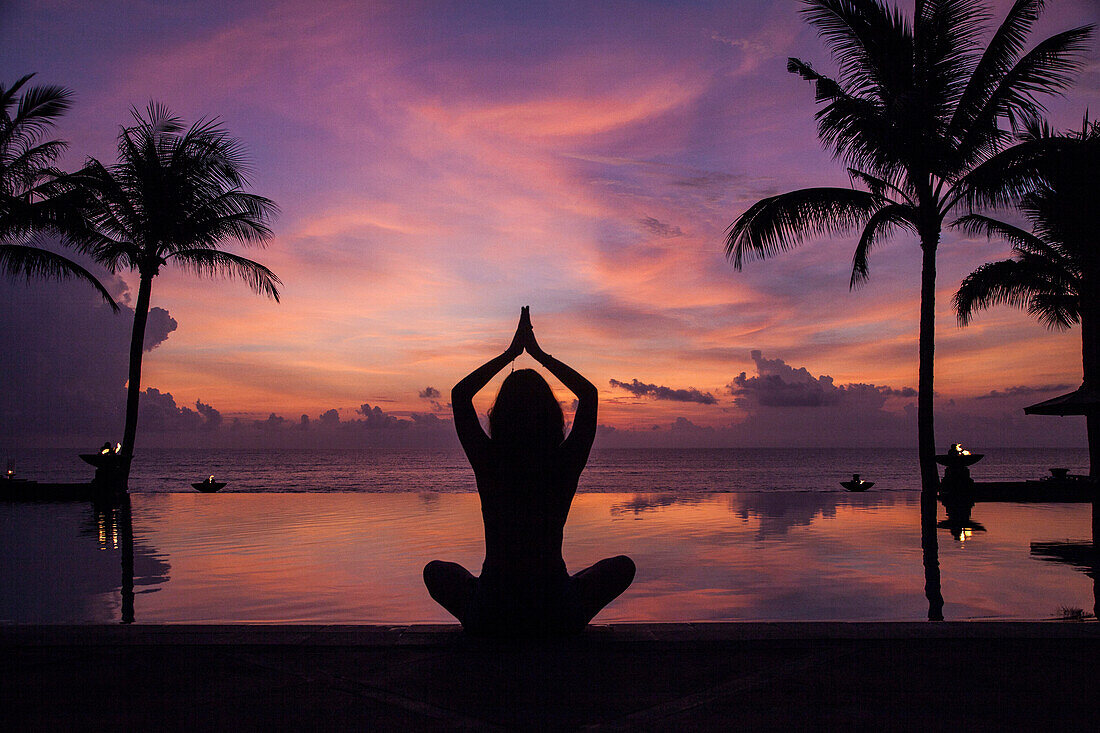 Silhouette einer meditierenden Frau am Swimmingpool bei Sonnenuntergang