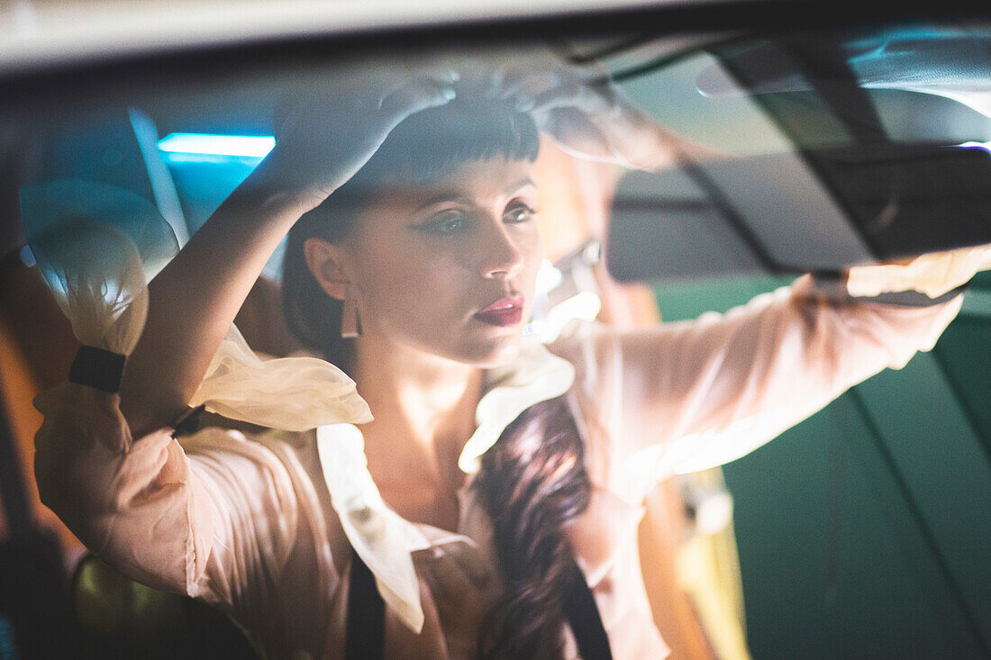 Glamorous mixed race woman checking hair in car mirror