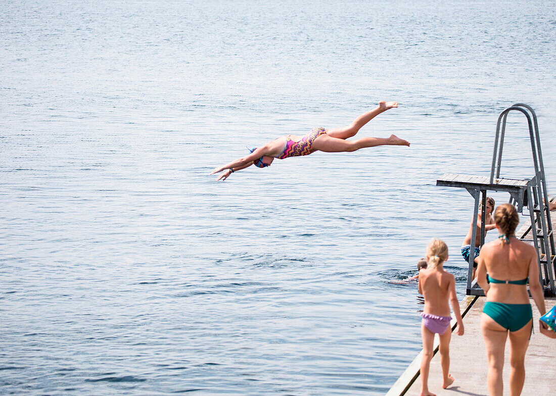 Caucasian girl jumping from diving board into lake