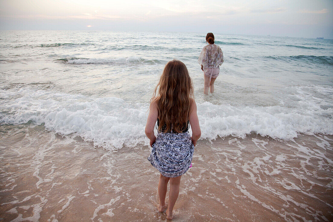 Mother and daughter walking in waves on beach