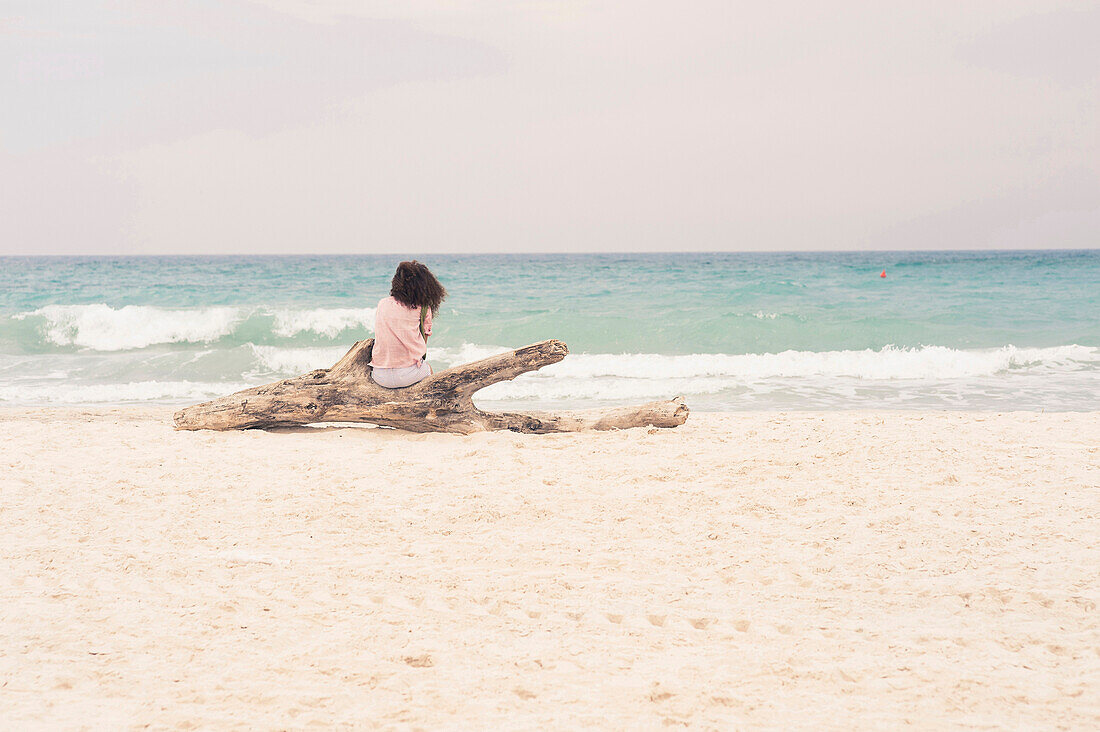 Frau sonnt sich auf einem Treibholzblock am Strand