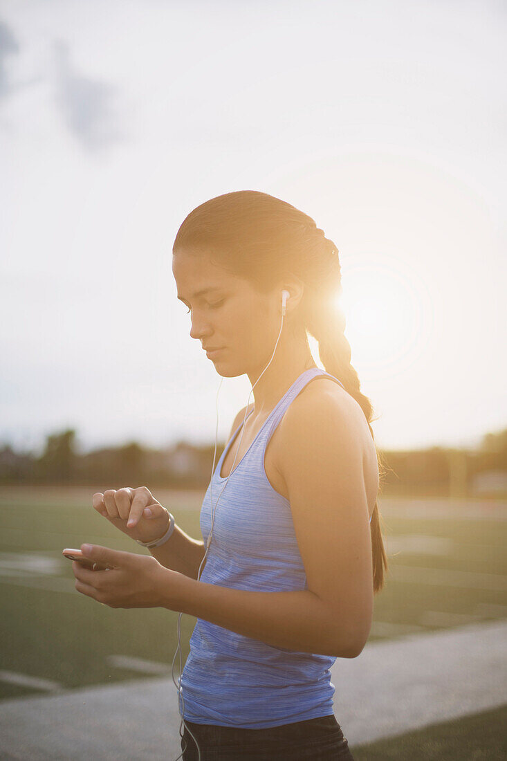 Gemischtrassiger Sportler hört auf einem Sportplatz einen mp3-Player