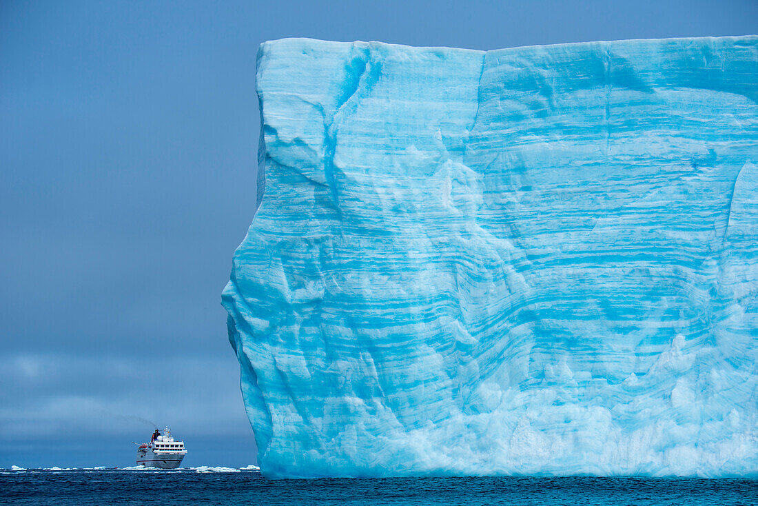Groessenunterschied: Expeditions-Kreuzfahrtschiff MS Hanseatic Hapag-Lloyd Kreuzfahrten hinter Eisberg, nahe Suedliche Orkneyinseln, Antarktis