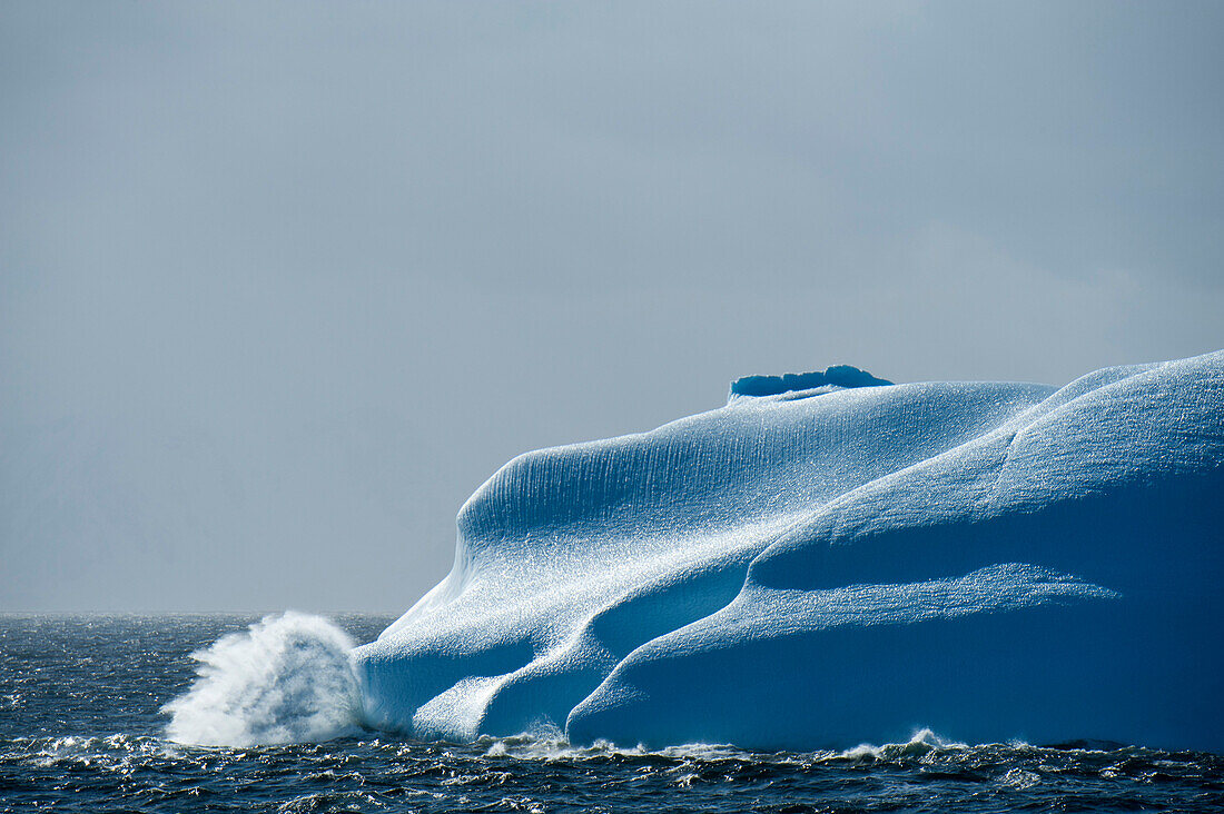 Wellen brechen an einem majestaetischen Eisberg suedlich vom Polarkreis, Westkueste, Antarktische Halbinsel, Antarktis