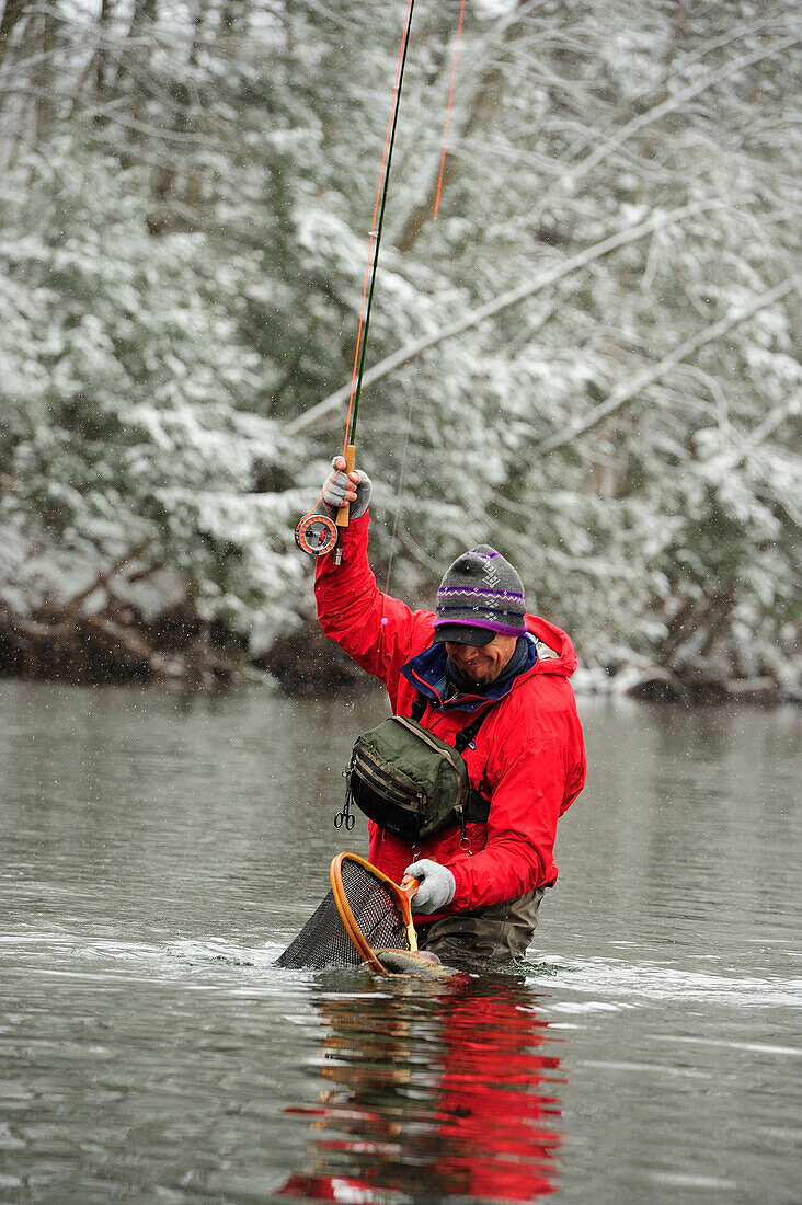 A man catches a trout on a cold, snowy day.