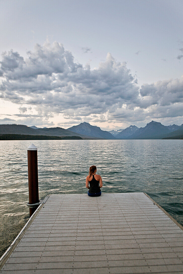 A young woman sits on the edge of a dock at sunset in Glacier National Park, Montana