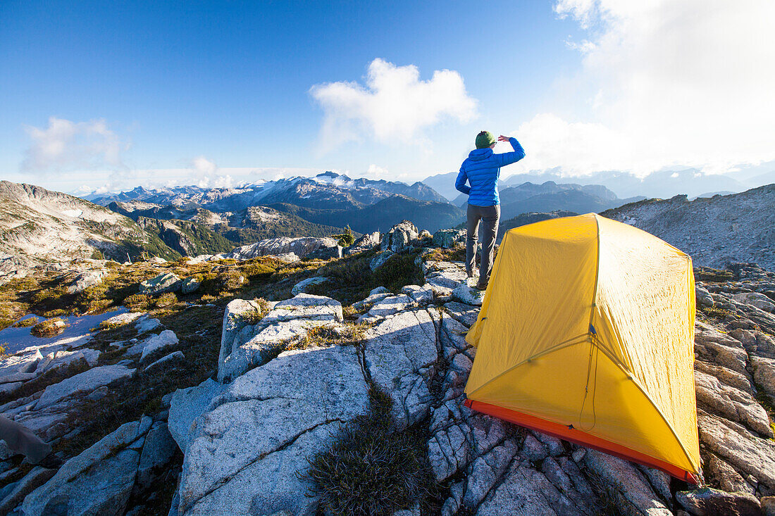 A young woman enjoys the view from her campsite on a rocky mountain ridge.