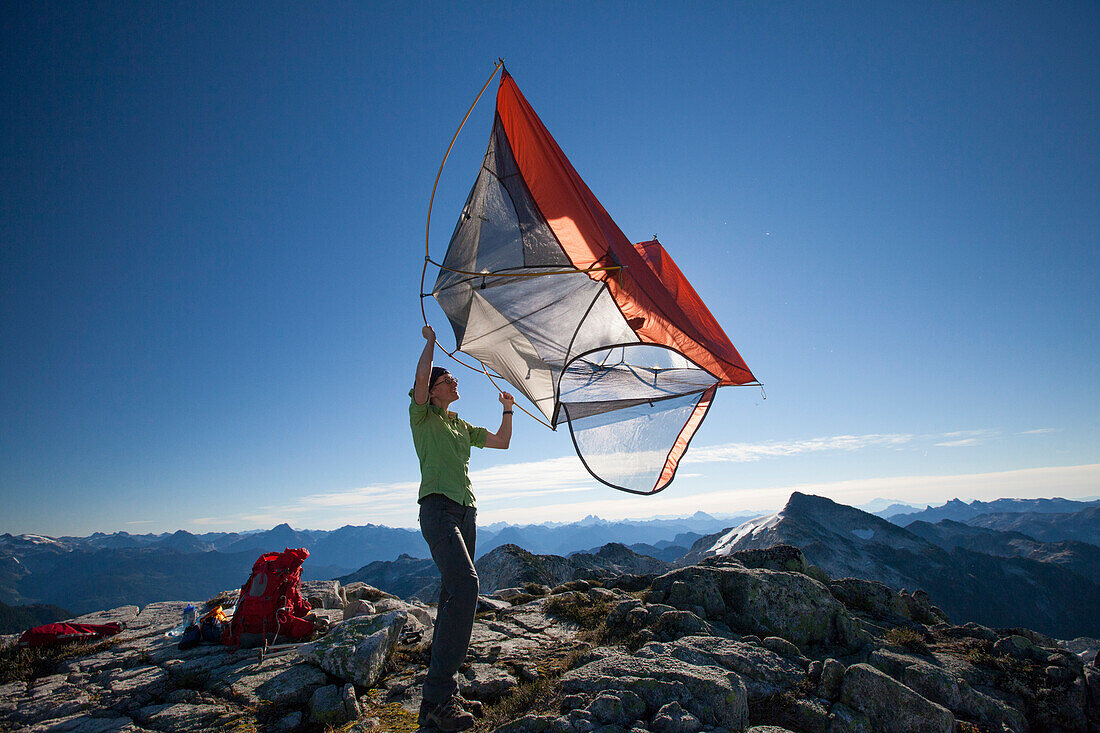 A female backpacker shakes the dirt out of her tent after camping on a rocky mountain ridge.