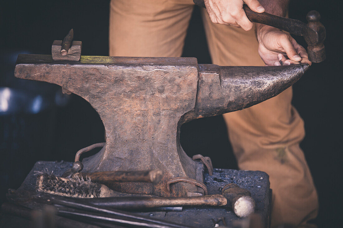 A blacksmith works on a large iron anvil.