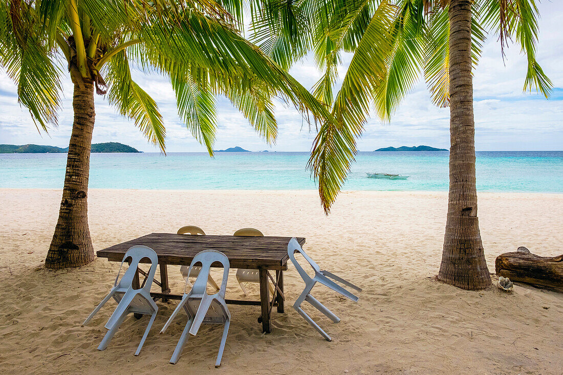 Palm trees and blue water on the white sand beach of Malcapuya Island