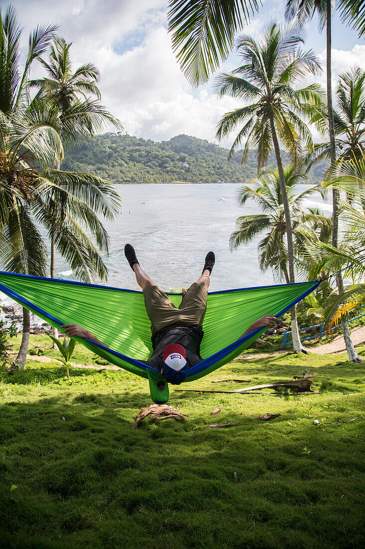 A young man swings in a hammock at Isla Grande, Panama, overlooking the ocean.