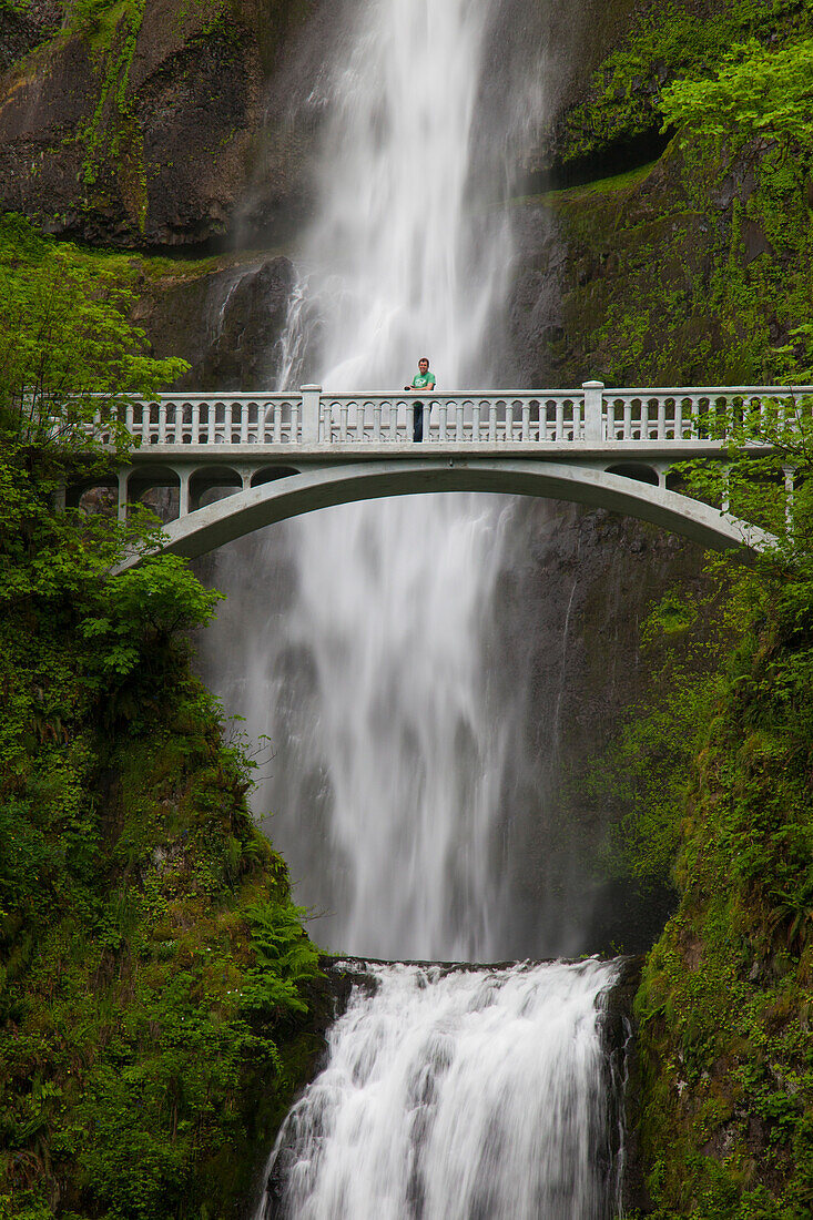 A man stands on the Benson Bridge in front of Multnomah Falls, a 542-foot waterfall located in the Columbia River Gorge, Oregon.