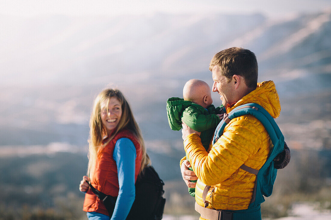 A young couple and their baby hike in the wintry mountains.