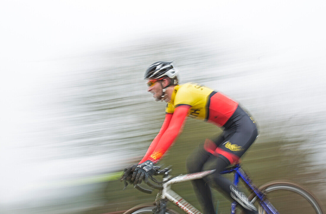 Blurred/Motion image of a male cyclocross racer at speed riding through a row or trees in a race.