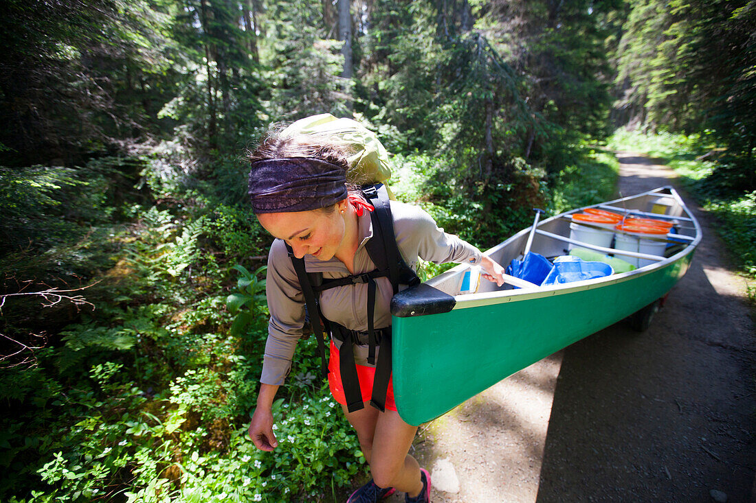 A young woman portages her canoe during a canoe trip through Bowron Lake Provincial Park.