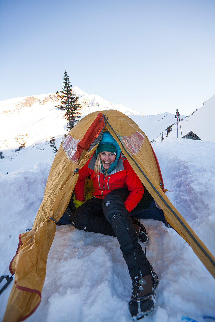 A young active woman poses for a picture in her tent while winter camping in British Columbia, Canada.