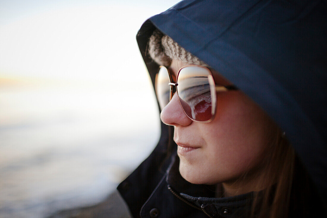 Portrait of a young woman wearing sunglasses and a hooded jacket while at White Rock Beach, British Columbia, Canada.