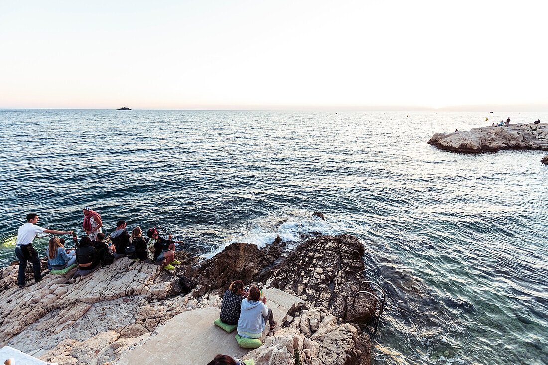 Young people sitting on rocks along the Adriatic coast, Rovinj, Istria, Croatia