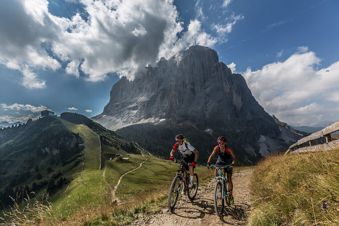 Mountain biker couple at the Ciampinoi, behind it Langkofel, Trentino South Tyrol, Italy