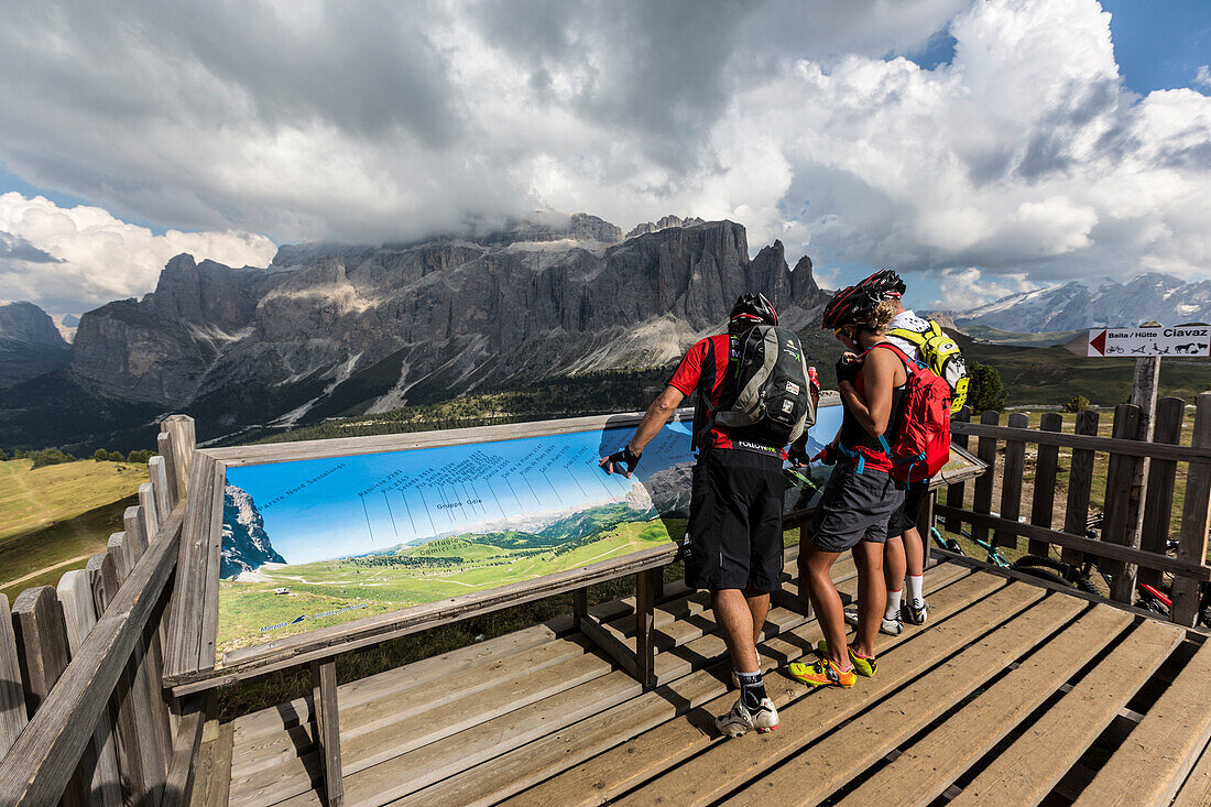 Mountain bikers in the Langkofel area standing at a panorama board, behind it Sella group, Trentino South Tyrol, Italy