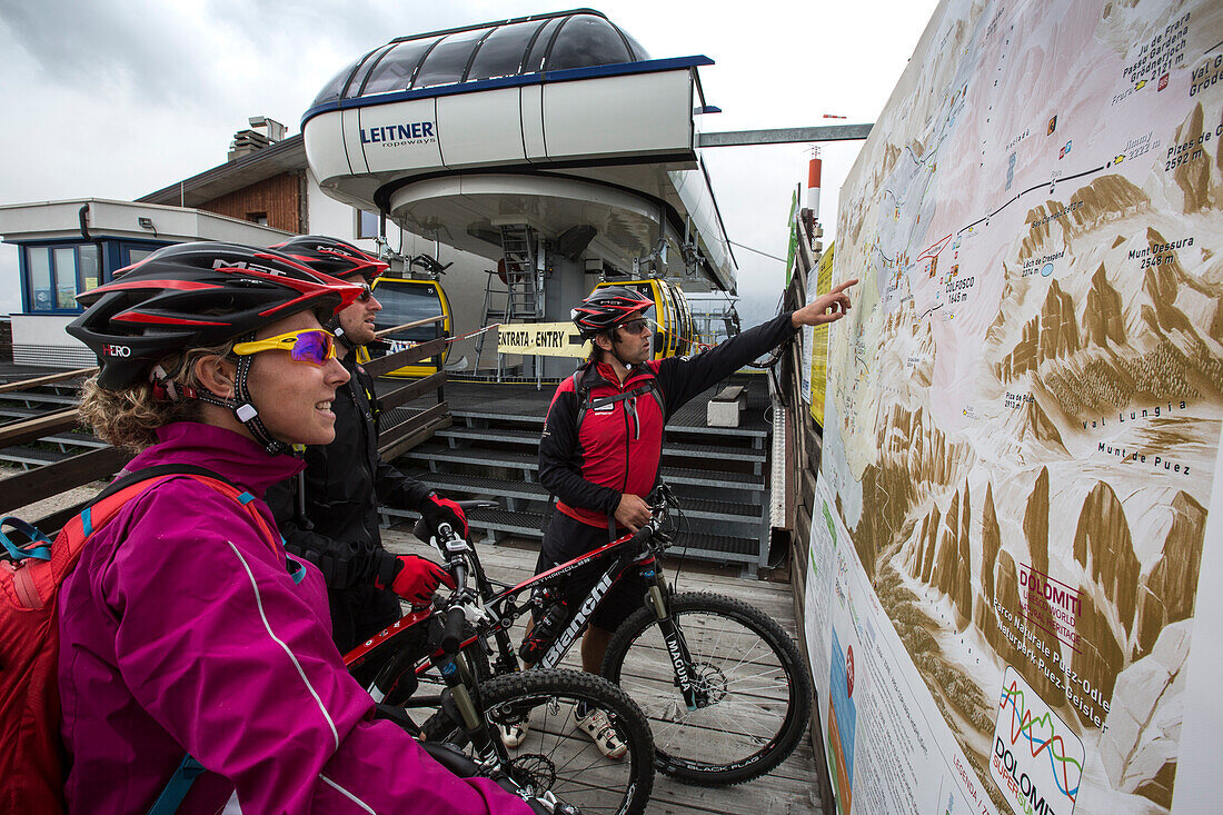 Mountain bikers looking at an environment map at the mountain station Col Alt, Corvara, Trentino South Tyrol, Italy